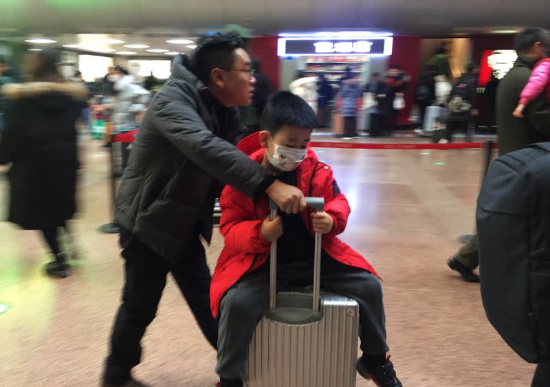 A man pushes his luggage as a child sits atop with a mask at the Beijing West Railway Station, in Beijing