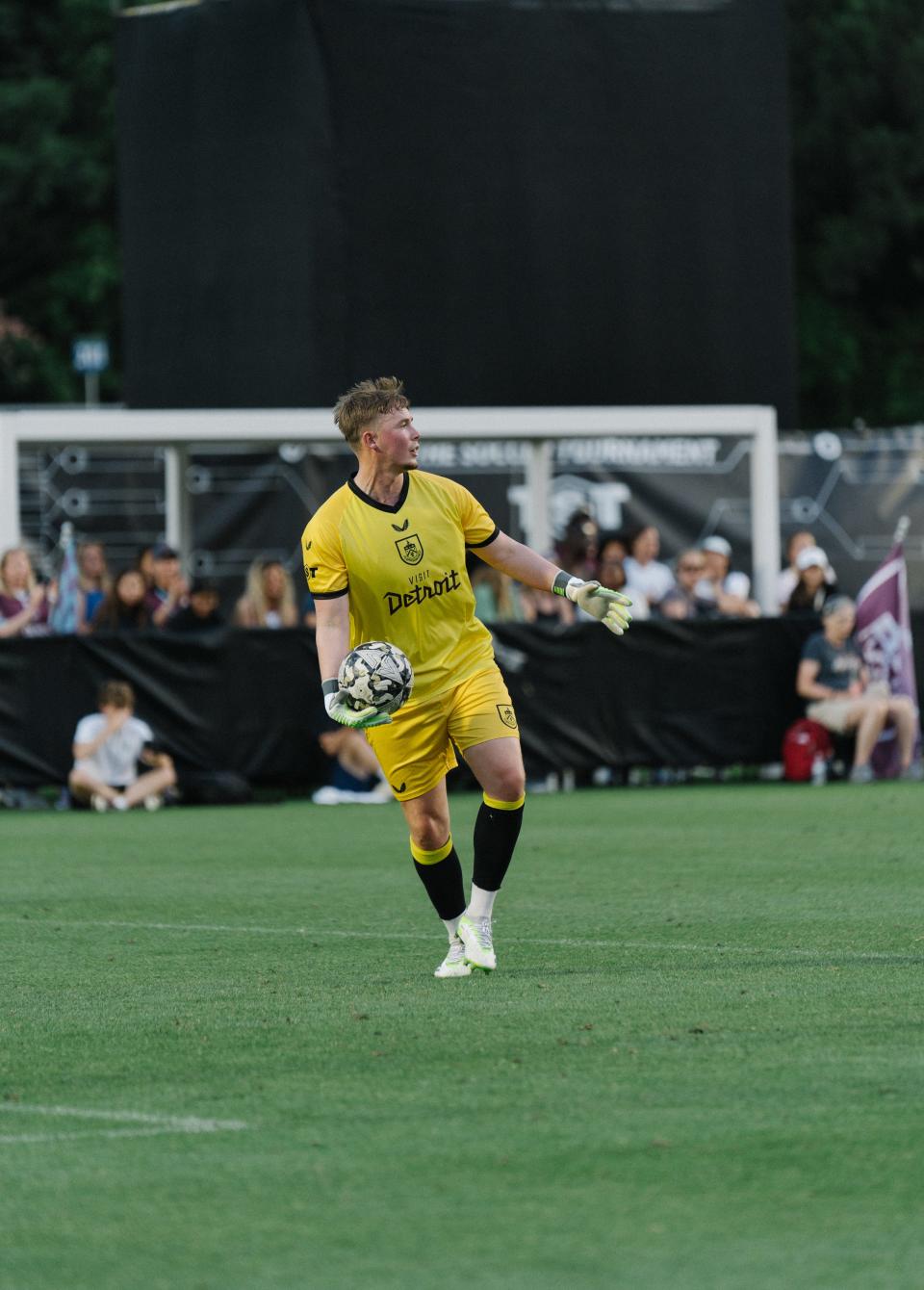 Burnley goalkeeper Connor King throws the soccer ball while wearing the alternate yellow Burnley jersey with the Visit Detroit sponsor on the chest.