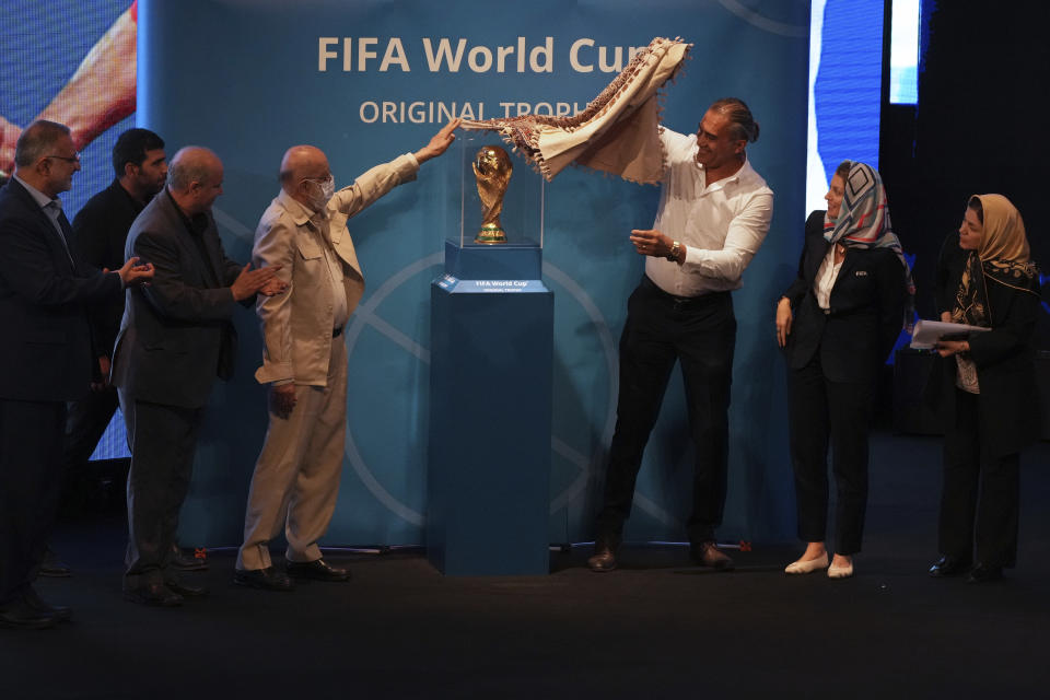 Tehran's city council chairman Mehdi Chamran, left, and former Iran's national soccer team captain Ahmad Reza Abedzadeh, right, reveal the FIFA World Cup trophy during the Trophy Tour, at Milad Tower hall in Tehran, Iran, Thursday, Sept. 1, 2022. Iran on Thursday put the FIFA World Cup trophy on display for the first time, part of the trophy's global tour ahead of the tournament that kicks off in neighboring Qatar in November. Sarah Gandoin of FIFA, second right, President of Iran's Football Federation Mehdi Taj, second left, and Tehran Mayor Alireza Zakani, left, stand on stage. (AP Photo/Vahid Salemi)