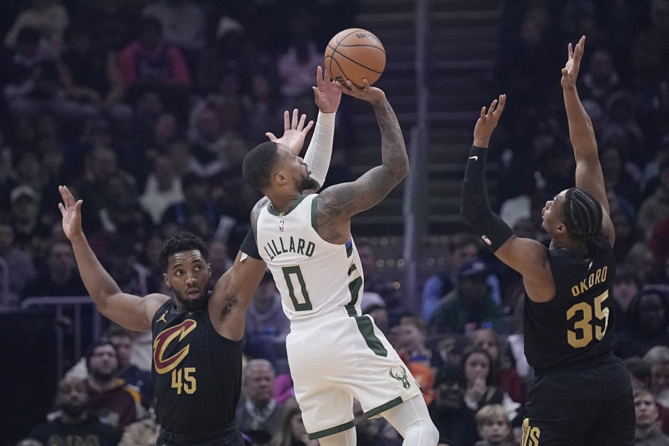 Milwaukee Bucks guard Damian Lillard (0) shoots from between Cleveland Cavaliers guard Donovan Mitchell (45) and forward Isaac Okoro (35) during the first half of an NBA basketball game Wednesday, Jan. 17, 2024, in Cleveland. (AP Photo/Sue Ogrocki)