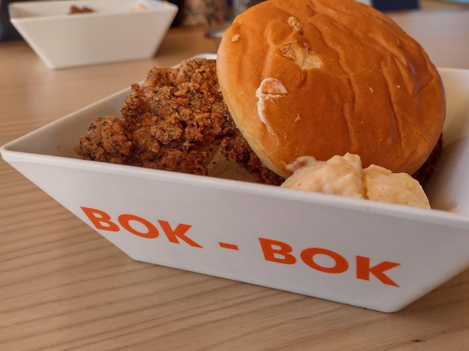 Shot of a burger bun and fried chicken in a white, square bowl with the words "bok bok" written in orange lettering.