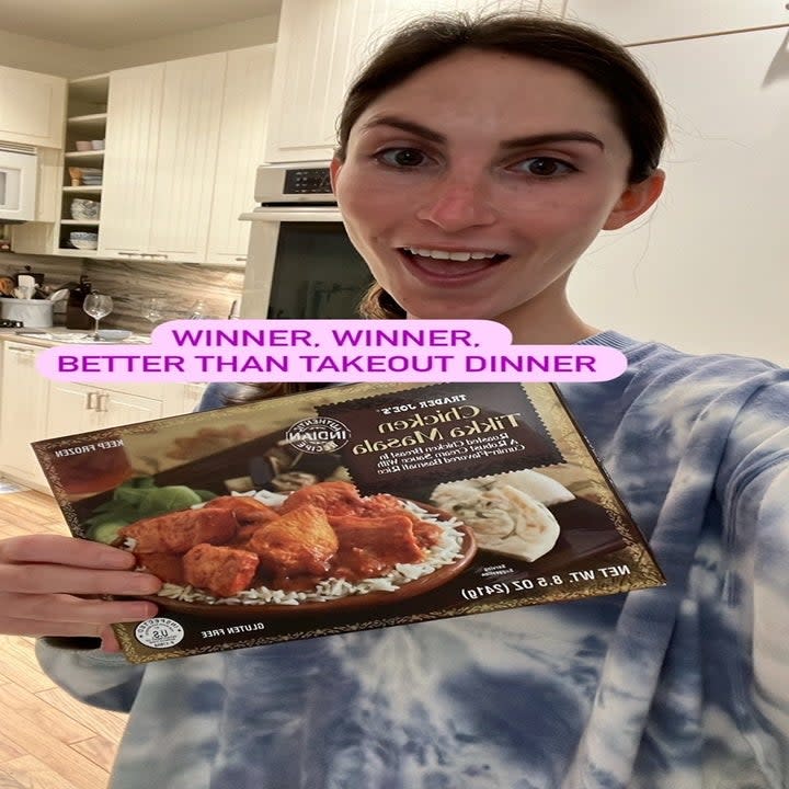 A woman holding a box of frozen chicken tikka masala.