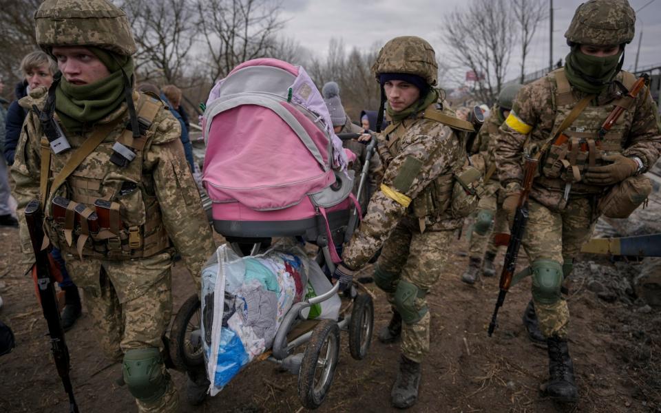 Ukrainian servicemen carry a baby pram after crossing the Irpin River on an improvised path under a bridge that was destroyed by a Russian airstrike, while assisting people fleeing the town of Irpin - AP Photo/Vadim Ghirda