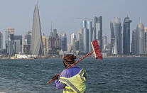 A worker walks at the Doha Corniche in front of the skyline on the day before the start of the Soccer World Cup in Doha, Qatar, Saturday, Nov. 19, 2022. (AP Photo/Martin Meissner)