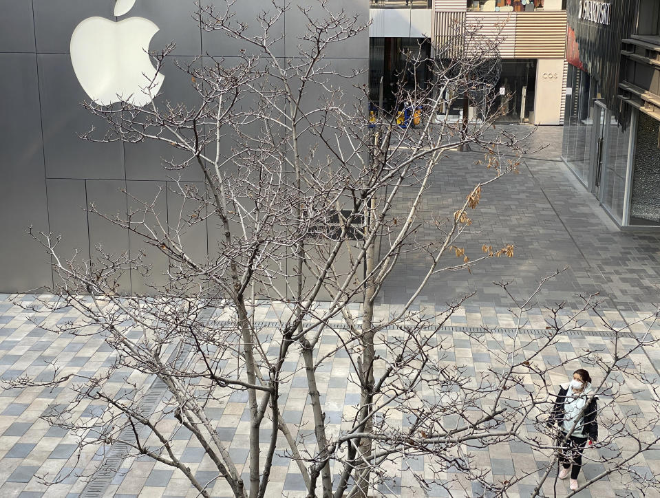 A woman wearing mask walks past the Apple store in an empty mall district in Beijing, China on Wednesday, Feb. 26, 2020. The tech giant Apple has reopened some of its stores in China but says the viral outbreak is starting to disrupt its supplies. (AP Photo/Ng Han Guan)