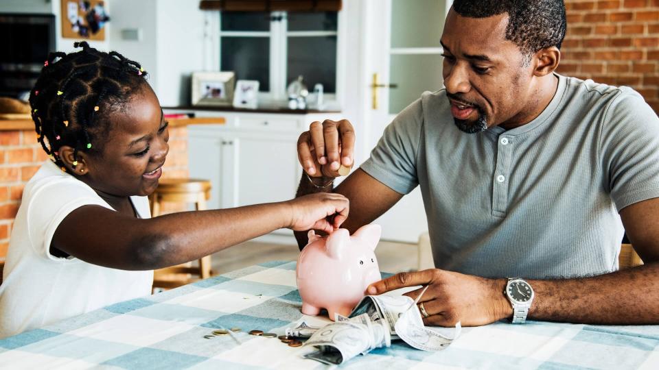 Dad and daughter saving money to piggy bank.