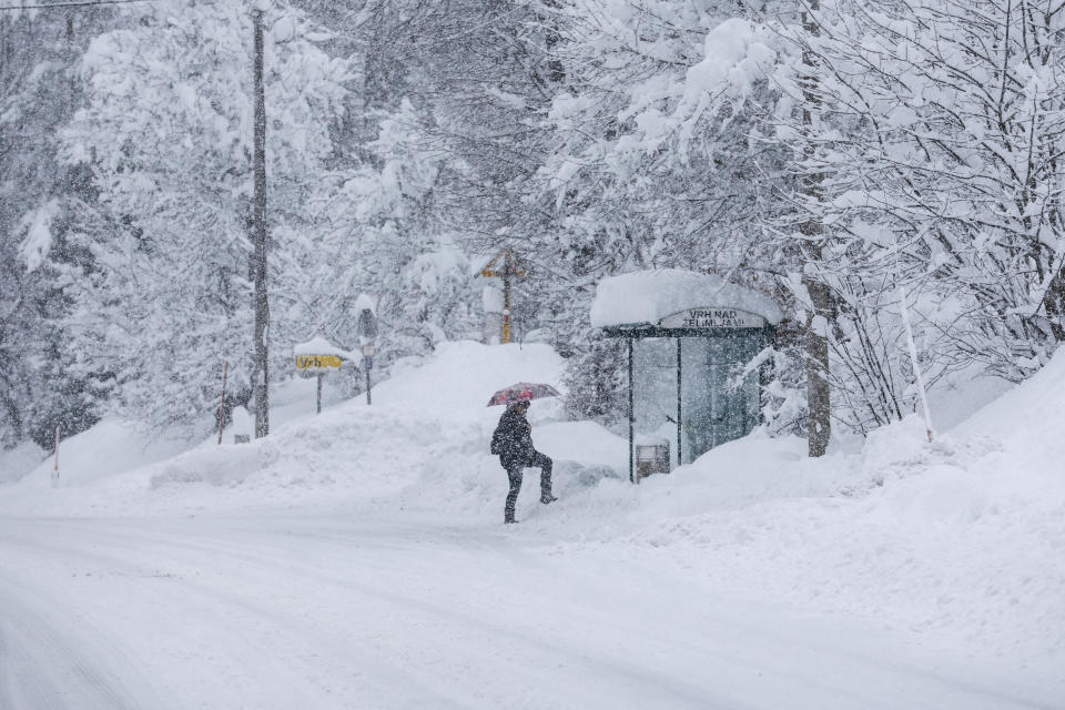 A person approaches a bus stop on a snow covered road in Kocevje, near Ljubljana Slovenia, Monday, Jan. 23, 2023. A snow storm with gust winds has hampered traffic on a key highway in Slovenia on Monday and left parts of the country temporarily without electricity. (AP Photo)