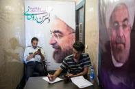 Men use their smartphones to follow election news as posters of Iran's President Hassan Rouhani are seen in Tehran, Iran May 17, 2017. REUTERS/TIMA