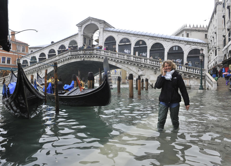 A woman walks in high water ner the Rialto Bridge in Venice, Italy, Thursday, Nov. 1, 2012. High tides have flooded Venice, leading Venetians and tourists to don high boots and use wooden walkways to cross St. Mark's Square and other areas under water. Flooding is common this time of year and Thursday's level that reached a peak of 55 inches (140 centimeters) was below the 63 inches (160 centimeters) recorded four years ago in the worst flooding in decades. (AP Photo/Luigi Costantini)