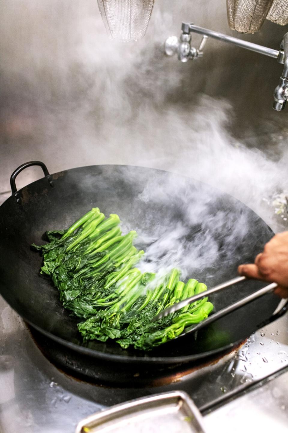 A cook sears gai lan at Cassia.