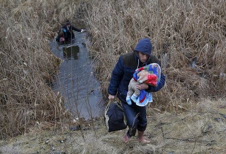 A Kosovar man wades through the water while carrying his child as they illegally cross the Hungarian-Serbian border near the village of Asotthalom, Hungary in this February 6, 2015 file photo. REUTERS/Laszlo Balogh/Files