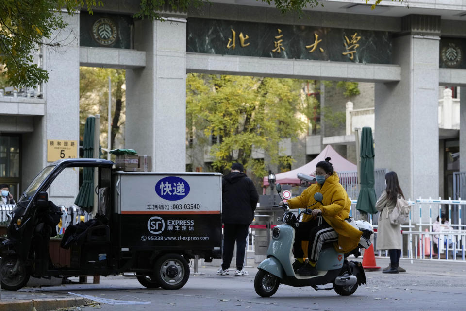A woman wearing mask rides past an entrance to Peking University in Beijing, Wednesday, Nov. 16, 2022. Chinese authorities locked down the major university in Beijing on Wednesday after finding one COVID-19 case as they stick to a "zero-COVID" approach despite growing public discontent. (AP Photo/Ng Han Guan)
