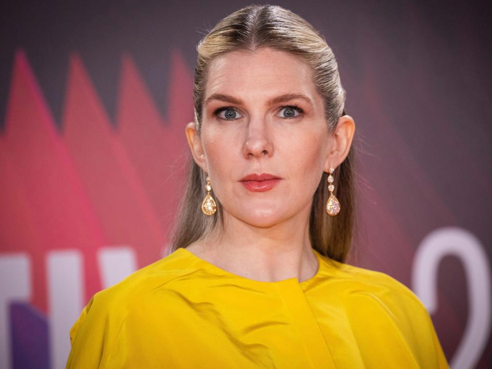 Lily Rabe wearing a yellow dress and gold drop earrings at a red carpet in October 2021.