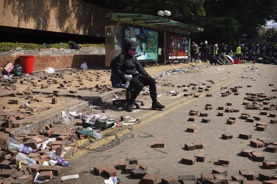 A protester rests near bricks scattered on a road near Hong Kong Polytechnic University in Hong Kong, Friday, Nov. 15, 2019. Protesters who have barricaded themselves in a Hong Kong university partially cleared a road they were blocking and demanded that the government commit to holding local elections on Nov. 24. (AP Photo/Vincent Yu)