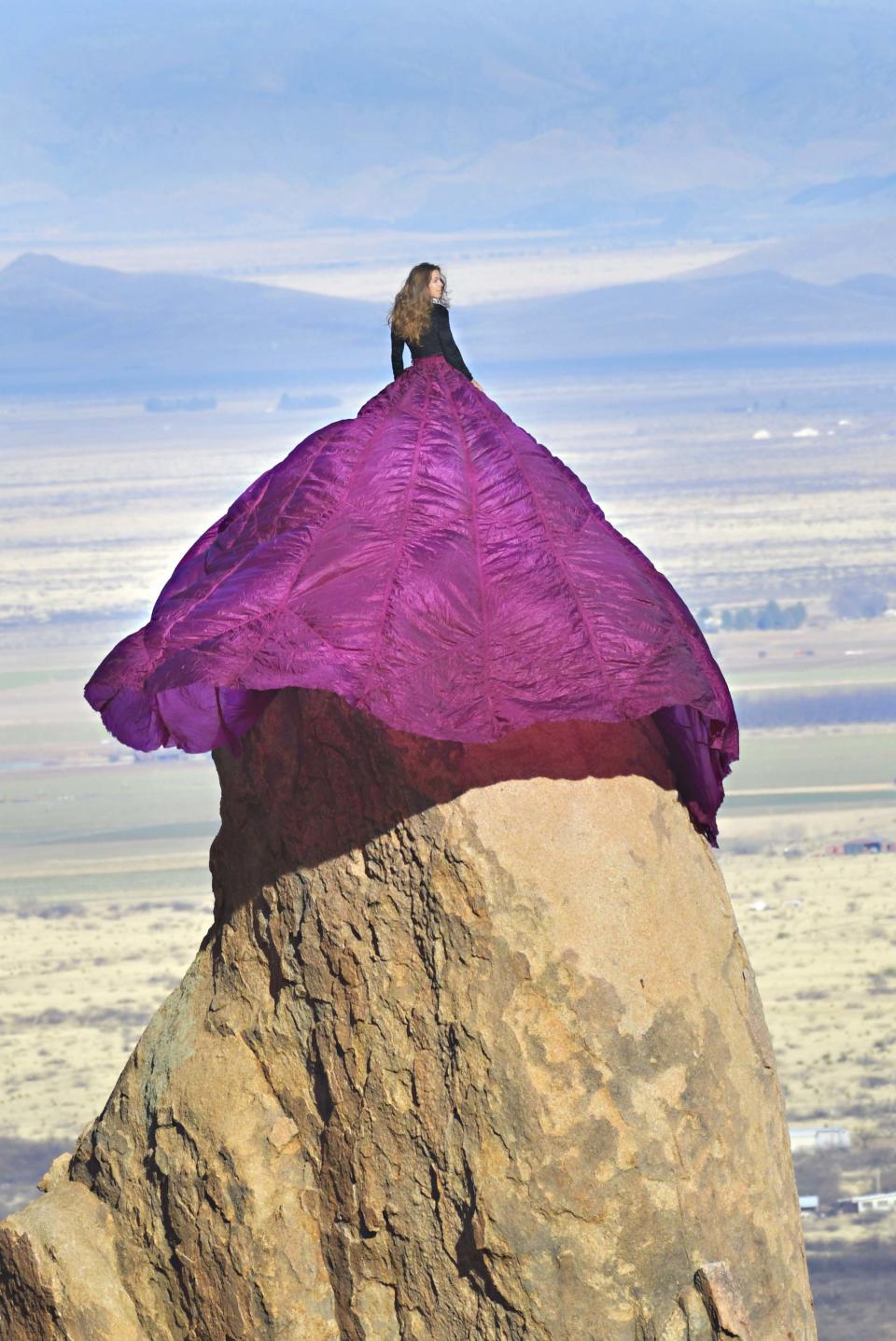 Dana Felker poses in huge purple gown atop a rock formation on the Dragoon Mountains, overlooking the Arizona desert, USA. 