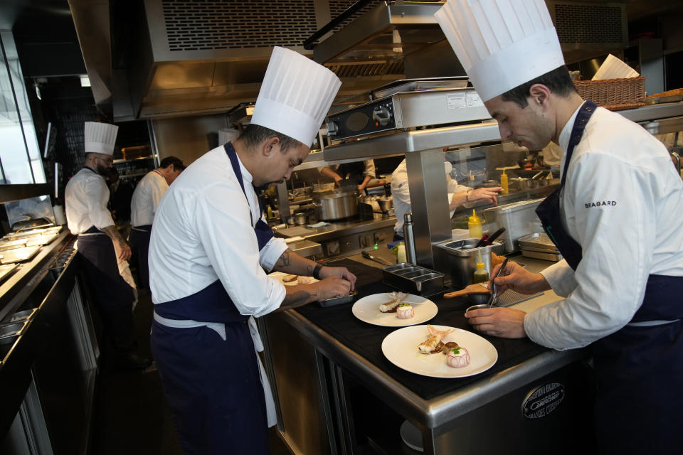 Cooks prepare food at La Tour d'Argent restaurant in Paris, Wednesday, Dec. 13, 2023. The Tour d'Argent, which claims to be the oldest restaurant in the French capital, has a front-row view of the renaissance of Notre Dame Cathedral as artisans prepare the fire-ravaged monument for reopening next year. The high-end restaurant, which helped inspire the movie "Ratatouille,'' recently reopened after its own renovation that preserved traditions while adapting to the 21st century. It will also overlook the opening ceremony of the Paris Olympics on July 26, 2024.(AP Photo/Christophe Ena)