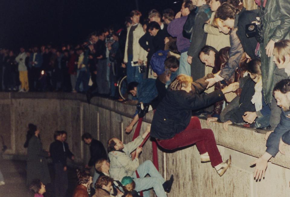 East Berliners get helping hands from West Berliners as they climb the Berlin Wall that divided the city near the Brandenburger Tor on November 10, 1989. The citizens facing the West celebrate the opening of the wall that was announced by the East German Communist government hours before.