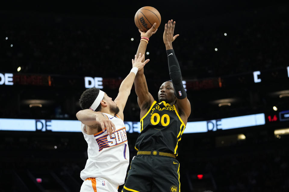 Golden State Warriors forward Jonathan Kuminga (00) shoots over Phoenix Suns guard Devin Booker during the first half of an NBA basketball game, Wednesday, Nov. 22, 2023, in Phoenix. (AP Photo/Matt York)