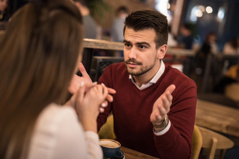 Two people in conversation at a cafe, with one person gesticulating and the other listening attentively