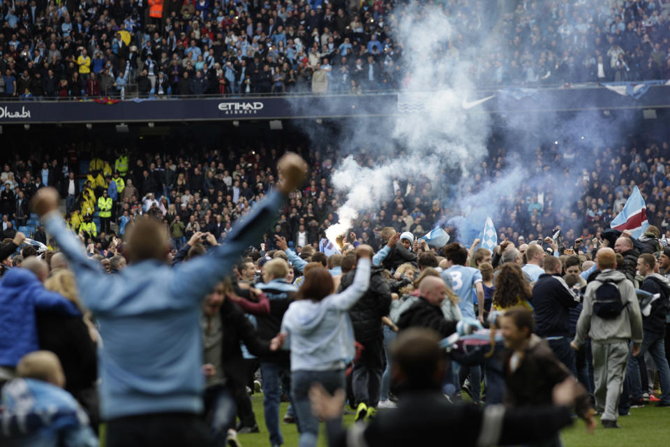 A flare is held up as Manchester City fans invade the pitch at the end of the English Premier League soccer match between Manchester City and West Ham at the Etihad Stadium in Manchester, England, Sunday May 11, 2014. Manchester City won the Premier League for the second time in three seasons on Sunday, completing its campaign with a comfortable 2-0 victory over West Ham that lacked any of the drama of its previous title. (AP Photo/Jon Super)
