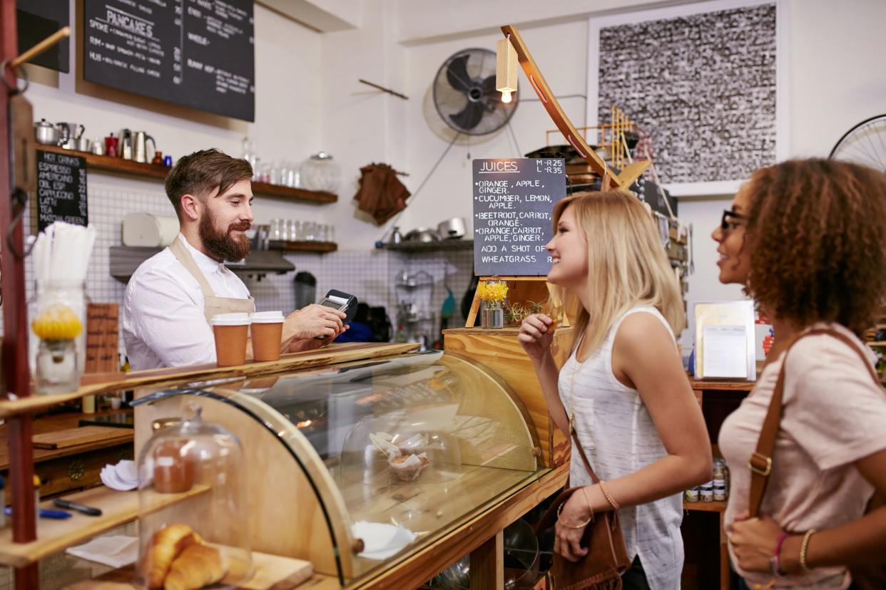 Shot of a young women friends placing an order in a coffee shop. Waiter taking coffee order from two young female costumers standing at cafe counter.