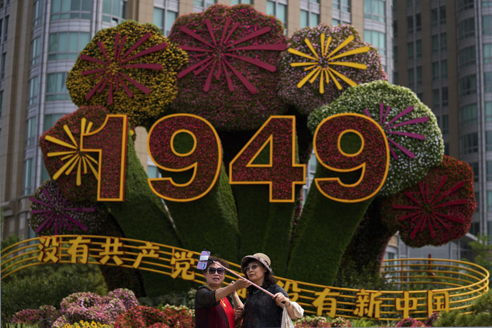 Chinese women take a selfie with a floral decoration caring the words "Without the Communist Party, There would be no new China" setup in Beijing, Monday, June 28, 2021. China is marking the centenary of its ruling Communist Party this week by heralding what it says is its growing influence abroad, along with success in battling corruption at home. (AP Photo/Andy Wong)