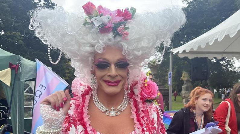 Magenta in full drag. She is wearing a pink flowery dress and a large white wig