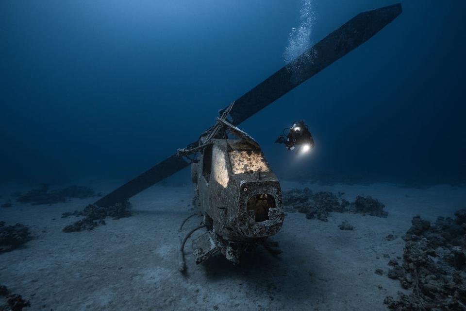 A Bell AH-1F Cobra helicopter sitting on the Red Sea floor off the coast of Jordan, its windows illuminated by the photographer.