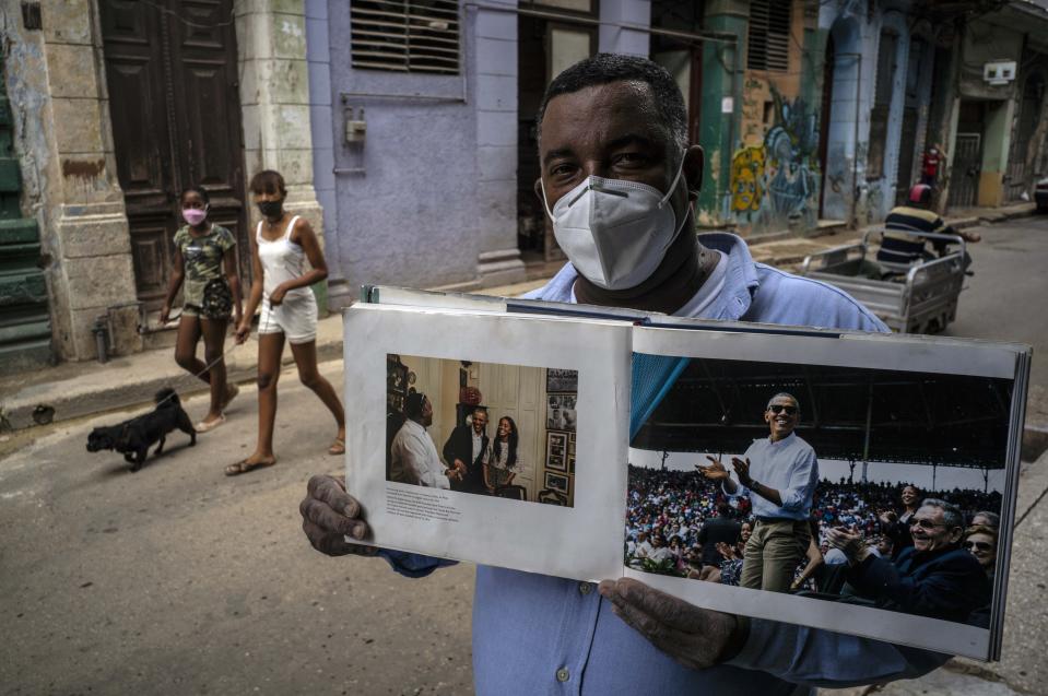 Wearing a face mask amid the new coronavirus pandemic, Cristobal Marquez, owner of "Cristobal's," the restaurant where Michelle and Barak Obama had lunch during their visit to Cuba in 2016, shows the book made by White House photographer Pete Souza, in Havana, Cuba, Thursday, Oct. 22, 2020. Obama restored diplomatic relations, loosened restrictions on travel and remittances and became the first U.S. chief of state to set foot in the island in 88 years. (AP Photo/Ramon Espinosa)