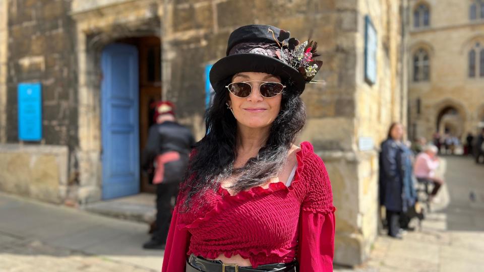 Woman dressed in red top with dark sunglasses and top hat decorated with feathers