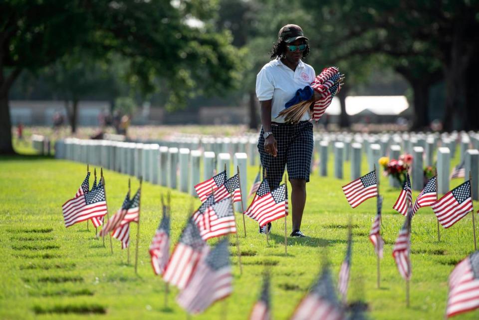 Volunteers help place thousands of tiny American flags on the graves of American service members at Biloxi National Cemetery in Biloxi ahead of Memorial Day on Saturday, May 25, 2024.