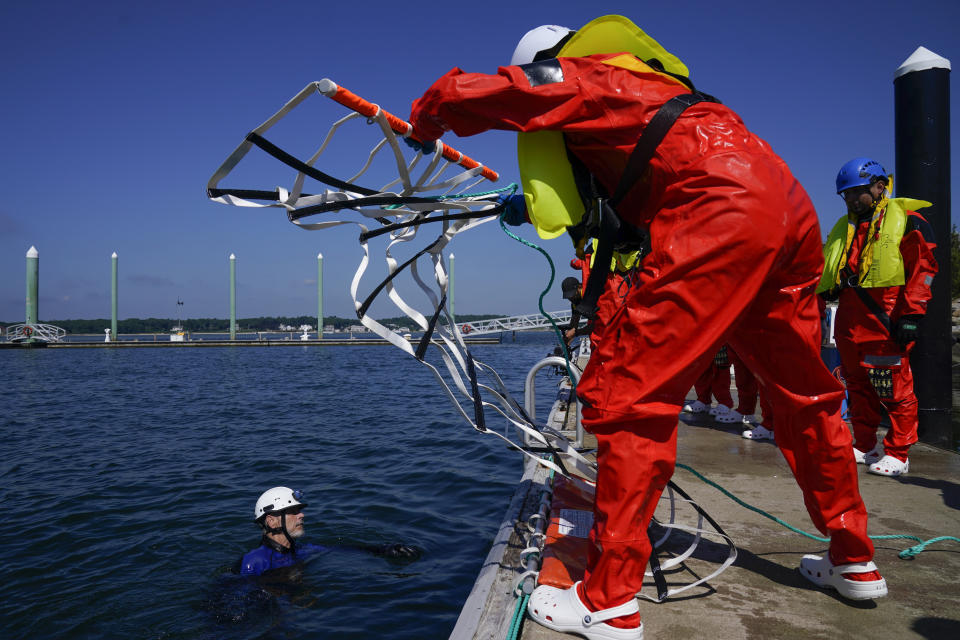 Instructor Stephen Faszcza, left, helps to demonstrate equipment used for water rescues during a Global Wind Organisation certification class at the Massachusetts Maritime Academy in Bourne, Mass., Thursday, Aug. 4, 2022. At the 131-year-old maritime academy along Buzzards Bay, people who will build the nation's first commercial-scale offshore wind farm are learning the skills to stay safe while working around turbines at sea. (AP Photo/Seth Wenig)