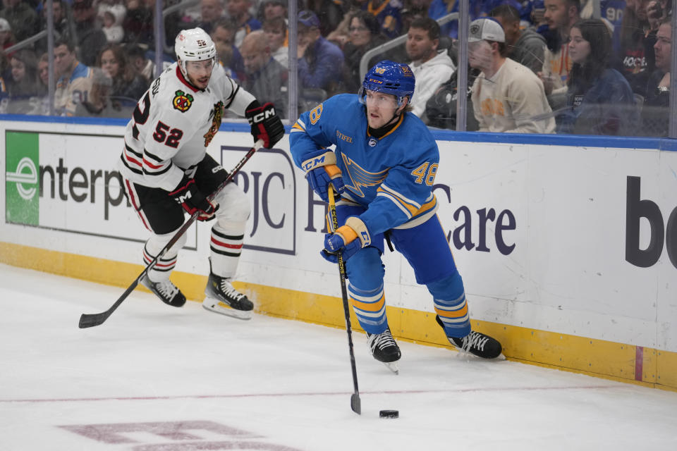 St. Louis Blues' Scott Perunovich (48) controls the puck as Chicago Blackhawks' Reese Johnson (52) watches during the first period of an NHL hockey game Saturday, Dec. 23, 2023, in St. Louis. (AP Photo/Jeff Roberson)