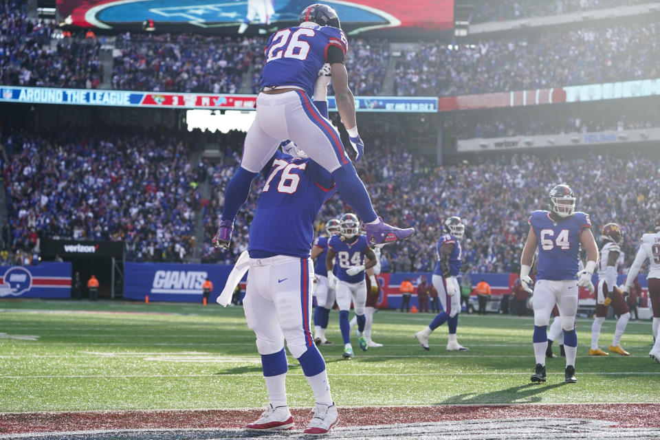 New York Giants' Saquon Barkley (26), top, celebrates his touchdown during the first half of an NFL football game against the Washington Commanders, Sunday, Dec. 4, 2022, in East Rutherford, N.J. (AP Photo/John Minchillo)