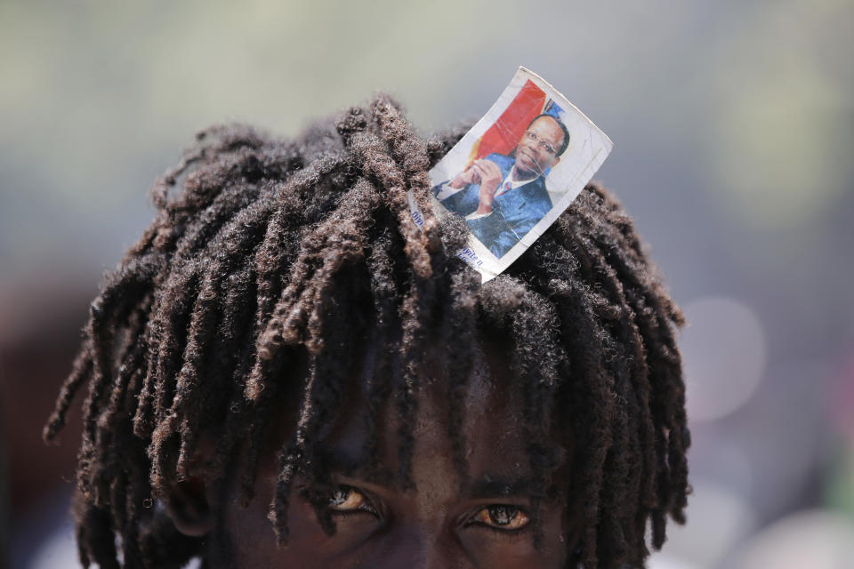 A supporter of former Haitian President Jean-Bertrand Aristide looks into the camera as he waits with others near the airport for his expected arrival from Cuba, where he underwent medical treatment, in Port-au-Prince, Haiti, Friday, July 16, 2021. Aristide's return adds a potentially volatile element to an already tense situation in a country facing a power vacuum following the July 7 assassination of President Jovenel Moïse. (AP Photo/Fernando Llano)