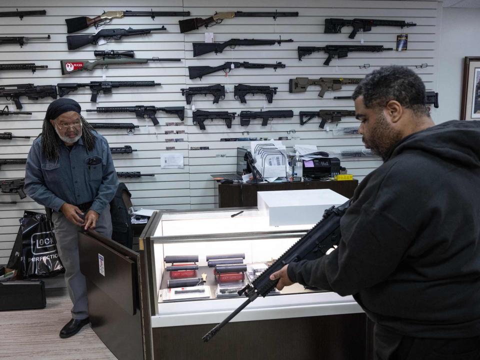 A man holds an AR-15 while the gun shop owner looks on at a Maryland gun shop