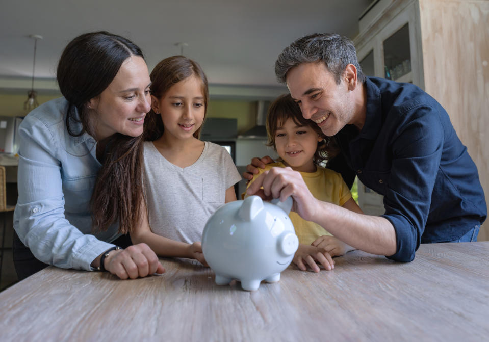 Loving latin american parents teaching their kids to save money in a piggy bank all smiling