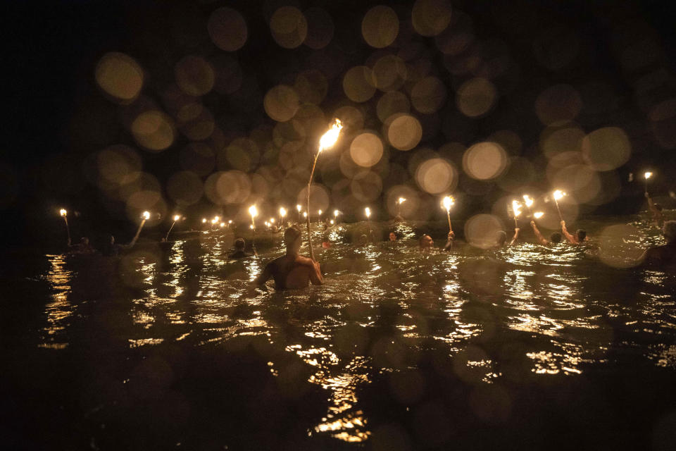 Salvavidas se meten en el mar con antorchas para conmemorar el Día del Salvavidas y honrar su compromiso con la seguridad y los rescates acuáticos, en Mar Azul, Argentina, el 14 de febrero de 2024. (AP Foto/Rodrigo Abd)