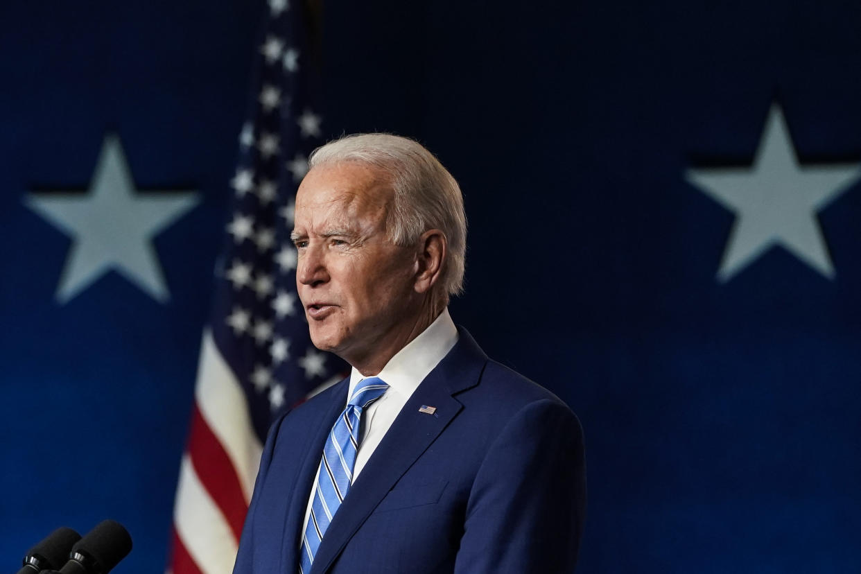 Joe Biden behind two microphones and in front of an American flag.