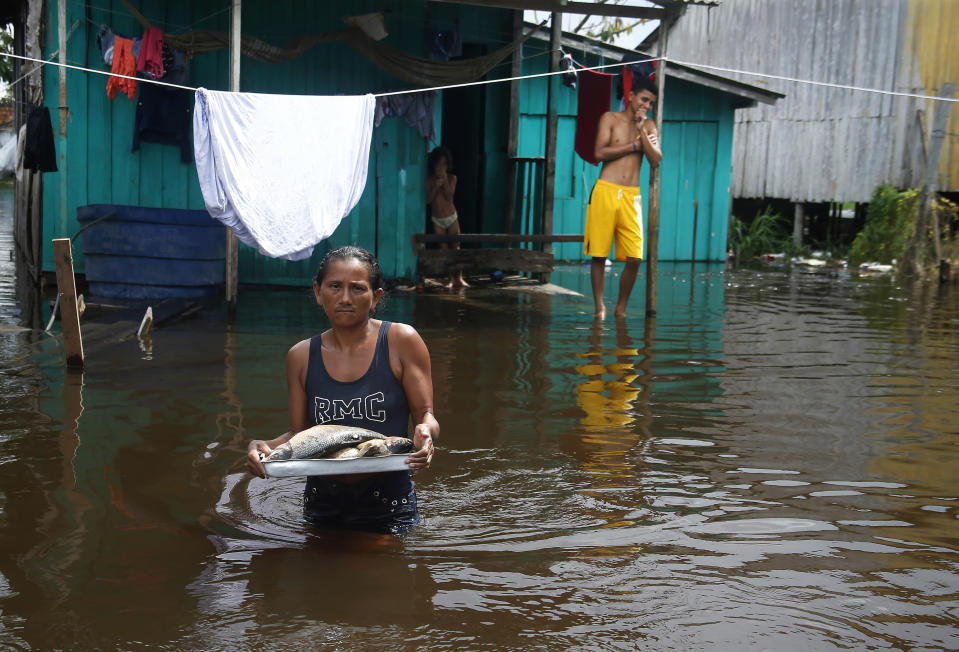 Edileuza Pereira da Silva carries a plate with fish for cooking outside her home, flooded by the rise of the Negro river in Iranduba, Amazonas state, Brazil, Monday, May 23, 2022. The Amazon region is being hit hard by flooding with 35 municipalities that are facing one of their worst floods in years and the water level is expected to rise over the coming months. (AP Photo/Edmar Barros)