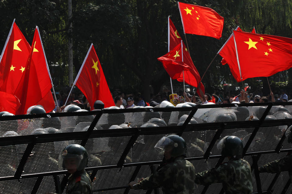 Anti-Japan protesters wave Chinese flags as they march outside the Japanese Embassy, guarded by paramilitary police in riot suits, in Beijing Sunday, Sept. 16, 2012. Security personnel outnumbered the crowds of Chinese protesting against Japan outside its embassy on Sunday, a day after demonstrations over islands that both nations claim spread across China and turned violent. (AP Photo/Alexander F. Yuan)