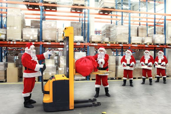 A group of Santas is shiw  in a shipping warehouse.