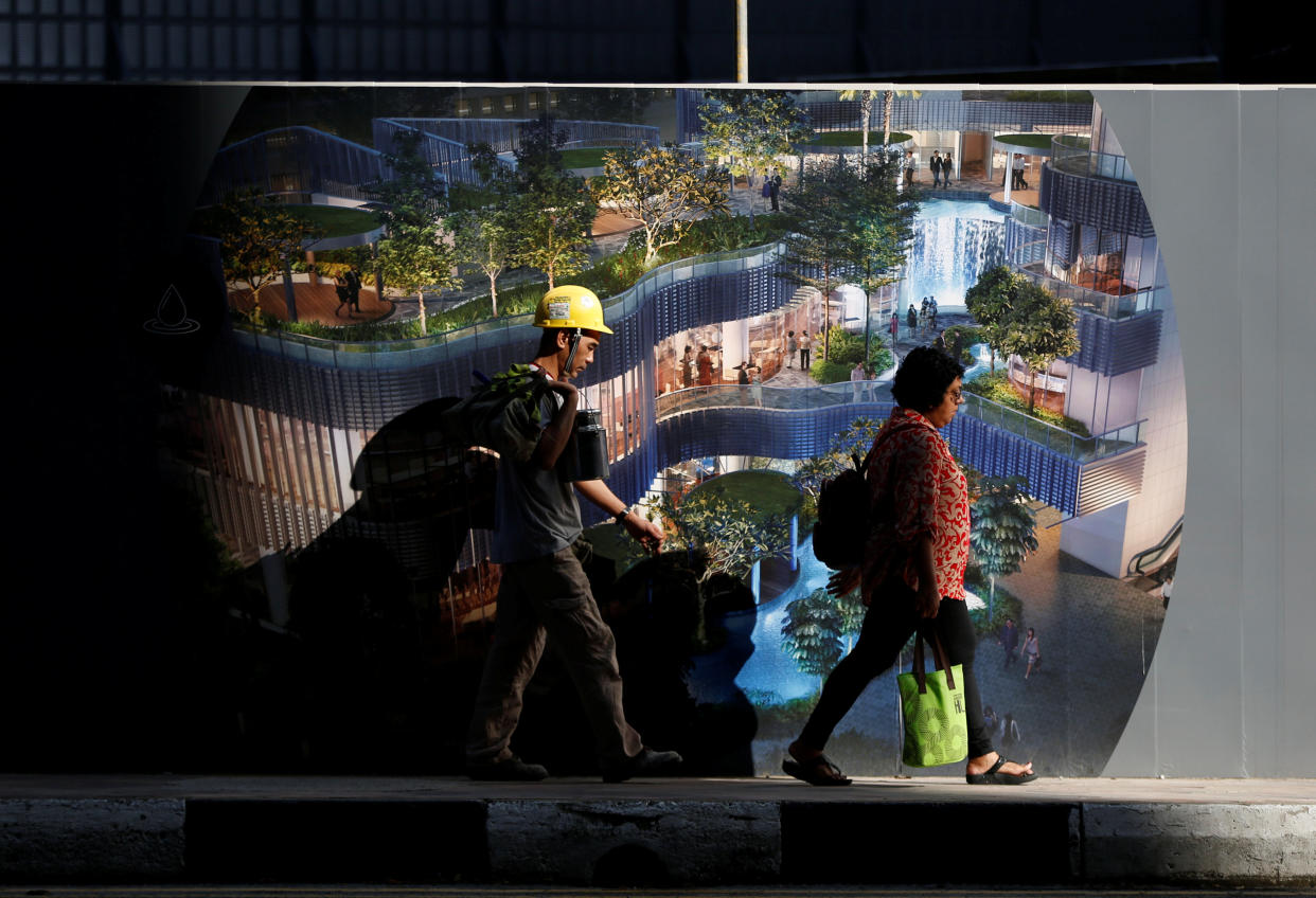 A construction worker and a pedestrian walk past a temporary wall at a construction site. (PHOTO: Reuters)