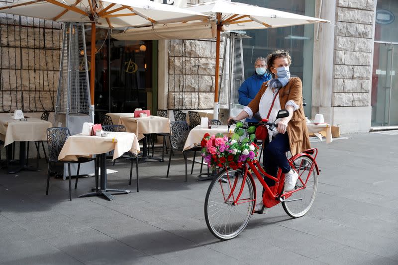 Una mujer con mascarilla pasa en bicicleta frente a la terraza de un restaruante en Roma