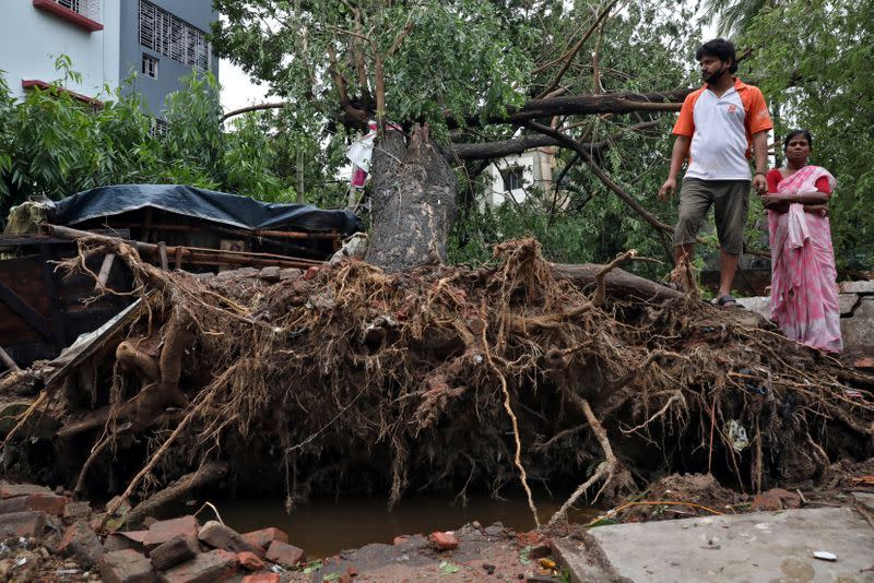 People stand next to an uprooted tree after Cyclone Amphan made its landfall, in Kolkata,