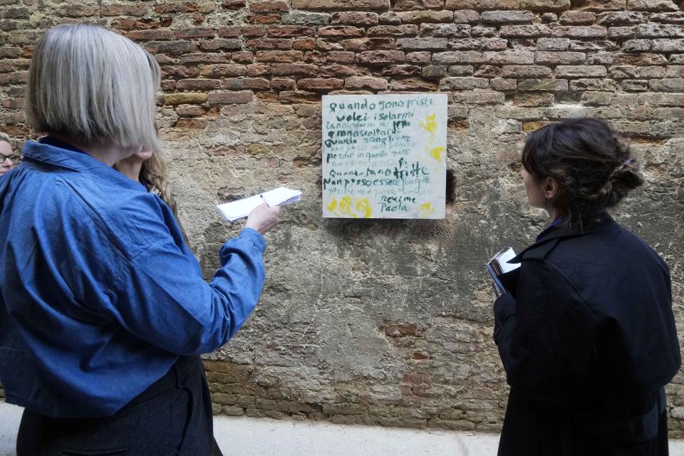 Reporters watches an installation by artist Corita Kent displayed inside the women's prison at the Giudecca island during the 60th Biennale of Arts exhibition in Venice, Italy, Wednesday, April 17, 2024. A pair of nude feet dirty, wounded and vulnerable are painted on the façade of the Venice women's prison chapel, the work of Italian artist Maurizio Cattelan and part of the Vatican's pavilion at the Venice Biennale in an innovative collaboration between inmates and artists. (AP Photo/Luca Bruno)