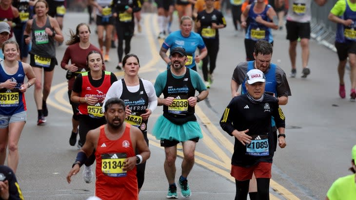Runners wearing costumes reach Heartbreak Hill and smile