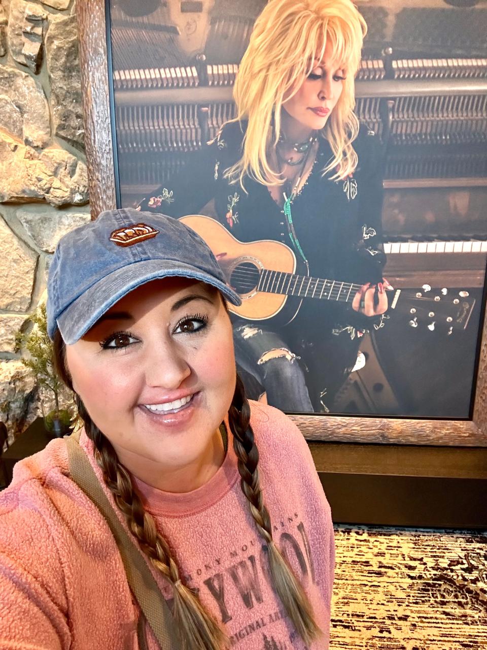 Author Carly Caramanna wearing a cinnamon bread hat and smiling in front of a framed portrait of Dolly Parton at HeartSong resort
