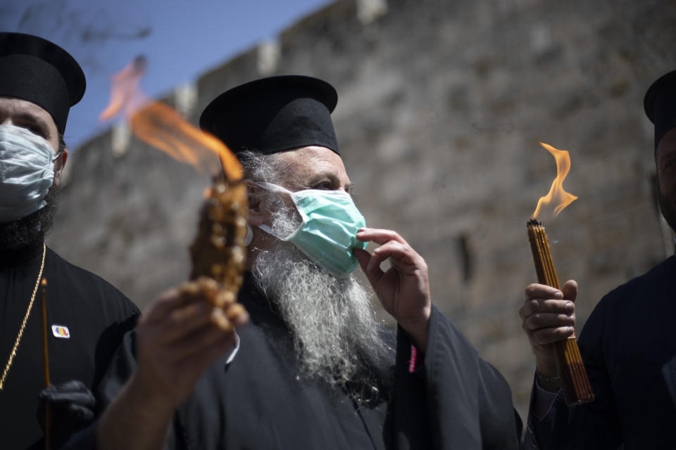 Orthodox clergymen hold candles lit from fire of the Church of the Holy Sepulchre, traditionally believed by many Christians to be the site of the crucifixion and burial of Jesus Christ, in Jerusalem's old city after the traditional Holy Fire ceremony was called off amid coronavirus, Saturday, April 18, 2020. A few clergymen on Saturday marked the Holy Fire ceremony as the coronavirus pandemic prevented thousands of Orthodox Christians from participating in one of their most ancient and mysterious rituals at the Jerusalem church marking the site of Jesus' tomb.(AP Photo/Ariel Schalit)