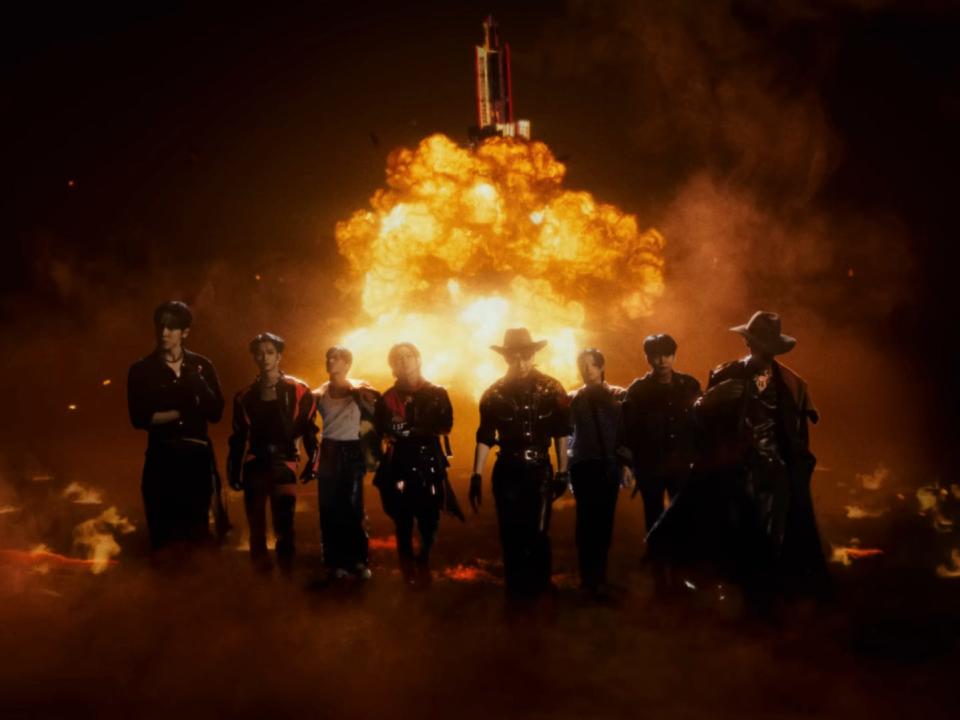 eight men dressed in a variety of outfits ranging from biker gear to outlaw outfits with cowboy hats walking away from a launching spaceship